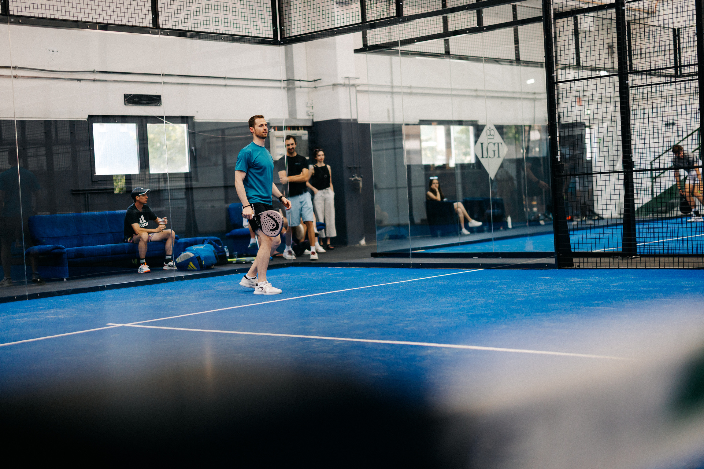 Spieler auf dem blauen Court, Zuschauer auf dem Sofa im Hintergrund